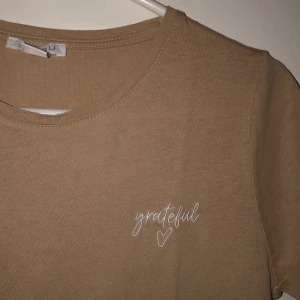 T-shirt från NewYorker - Beige t-shirt i nyskick. Aldrig använd. Texten ”grateful” på bröstet. Frakt är inkluderat i priset.