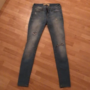 Hollister jeans - Tajta, lågmidjade, blåa jeans från hollister. Slitningar på båda benen. 