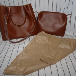 Cognacfärgad handväska - Helt ny med plasten och etikett kvar, skinnimitation, mjuk tyg på insidan, korta handtagen är robusta i stadig metall, följsam dragkedja. Ångrade köpet men internationell retur kostade nästan mer än väskans ord.pris (450kr), säljer därför här! Kan skicka fler bilder 🥰