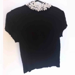  - Festlig svart topp med dekorativ polo. Vita detaljer. Kortärmad. Fint skick! 