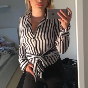 NA-KD blus  - Supersnygg blus från NA-KD i väldigt bra skick, säljes pga alldeles för liten för mig vilket ni nog ser! Det är fyra knappar framtill, rosetten på magen går att knyta upp och knyta bak om man hellre vill ha det så!🥳 