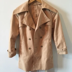  - Beige vårkappa. 60-70-tal. Köpt secondhand och uppsydd av tidigare ägare. Skärp i midjan. Vänster till höger knäppning. Upphämtas i Göteborg eller skickas mot att köparen betalar frakten. 