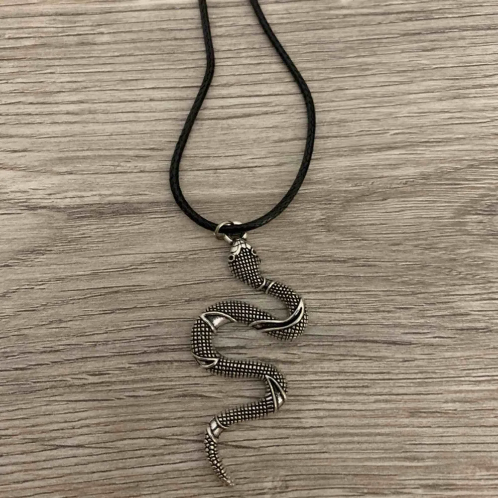 Coolt halsband med hänge i form av en orm. Ormen är i silverfärgad metall och har fina mönster i sig. Sitter på ett läderband. . Accessoarer.
