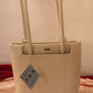 Zack axel/ryggväska  - Jättefin vit axel/ryggväska från ZACK köpt i butik. Helt oanvänd med produktlapp kvar. Kan bäras på axel eller rygg. Vit läderimitation med stort innerfack samt två mindre fack med dragkedja.  Nypris 399. Pris 200 kr+ev frakt. Finns i Sthlm/Uppsala 