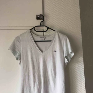 - Plagget jag säljer är en vit med en liten nyans av ljusblå Lacoste t-shirt i storlek 34, knappt använd. 