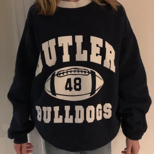 Mörkblå sweatshirt med tryck - INTRESSEKOLL!! Funderar på att sälja min mörkblå sweatshirt från Beyond Retro. Köpte den för ca 1 år sedan och är i jättebra skick!!! Den har vitt tryck på både fram och baksidan. På framsidan står det.  ” Butler Bulldogs ” och har en amerikansk fotboll med talet 48 i mitten. På baksidan finns ett tryck av en bulldog. Skulle säga att den sitter som en S-M. Den är väldigt oversize på mig som är ca 165. Möts antingen upp på Östermalmstorg eller i Slussen eller så skickas tröjan med posten. Budgivning startar vid 200 + frakt. Man måste buda minst 10kr mer än förra budet.
