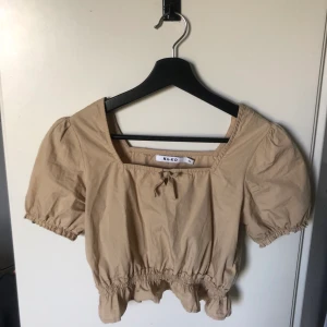 Kort topp NAKD storlek 32 - Söt topp i beiget från NAKD i storlek 32, skit snygg till ett par blåa högmidjade jeans, true to size
