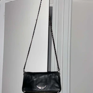 Zadig och Voltaire väska - Rock Bag Svart - Svart väska från Zadig & Voltaire i den större modellen. Väl använd därav billigare pris. Originallpris 3300kr, mitt pris från 800kr. Den korta kedjan finns kvar men är trasig i spännet och det finns ett litet hål inuti väskan, det syns inte utanpå såklart!