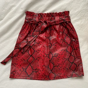 Kjol - Cool kjol i rött snakeprint och pu-läder. Storl M men eftersom den har ett snöre går det att anpassa storleken. På insidan är det ett mjukt material som ger lite värme. Har inte använts fler än 3 gånger och är därför i nyskick. Självklart går det att buda💕