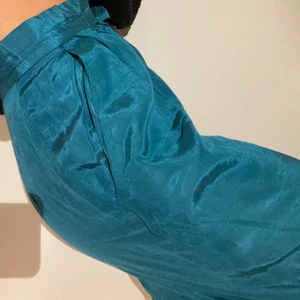 Turkosa kostymbyxor - Turkosa byxor i silkesliknande material i kostymbyxe-modell! Fickor finns och det går att enkelt du till en knapp om en vill det -(annars är dragkedjan självlåsande efter att ”flärpen” tryckts ner). Det finns några små noppror men de läggs inte märke till.