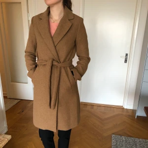 Ullkappa Bershka NY - Säljer denna superfina ullkappa eftersom den är för liten för mig. Har bara använts ett fåtal gånger. Är storlek S men ganska liten upptill så kanske bättre till en person med XS. Hällorna till skärpet är tunna så den går även bra att ha utan skärp. Material: 72% polyester, 22% ull, 6% andra fibrer. Köparen står för ev frakt.