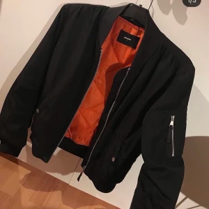 Svart bomberjacka   - Svart bomberjacka från Bikbok med orange foder inuti. Frakten är inräknad i priset.