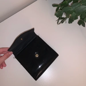 Mini väska - mini väska/plånbok i svart lackat material! köpt på secondhand butik! dock lite sliten på baksidan (se bild 3), men inget stort! köparen står för frakten🦋 3 för 2!