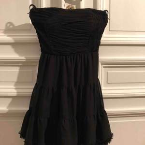 Kort svart klänning med korsett överdel och vid kjol. Dragkedja i sidan och resår bak.