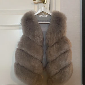 Grå fuskpälsväst - Grå fuskpälsväst i storlek M, använd 1 gång,har hakar på insidan så man kan stänga den om man skulle vilja det! Är 173 och brukar ha S/M