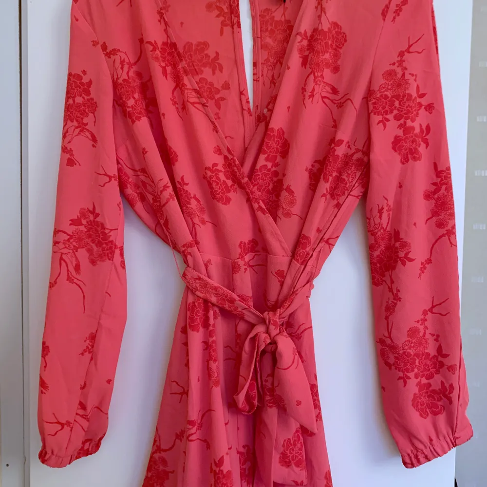 Rosa jumpsuit med röda blommor, öppna ärmar och knyte i midjan 🌺 den är ganska urringad i bröstet men det finns en knapp så man kan knäppa till. Använd fåtal gånger, bara att höra av sig om bild på önskas 🌷. Klänningar.