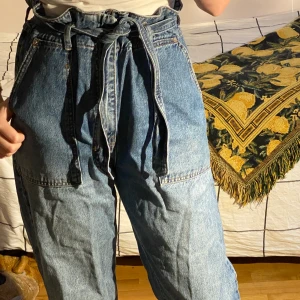 Jeans med knyte, Gina Tricot stl 38-40 - Jeans med knyte från Gina i storlek 40. Jag köpte dem på Tise, men säljer dem då de är lite för stora för mig och inte riktigt kommer till användning. De passar även storlek 38 då midjan är justerbar. De är i fint skick och inget fel på dem, färgen är lite mer blå i verkligheten. Skriv privat om du är intresserad eller har frågor,  Samfraktar gärna vid köp av flera plagg. ✨