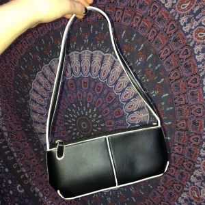 Svart mini-handväska med vita kontrastlinjer - Liten jättegullig handväska med fina vita linjer som blir kontrast till den svarta färgen! Köpt second hand för ca ett år sen men använd sällan. Troligen från 2000-talet men ändå fint skick. Köparen står för frakt!<3