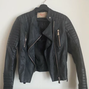 Skinnjacka från Chiquelle  - Mc-inspirerad jacka i läderimitation med quiltade detaljer på axlar och i ärmslut. Två fickor med dragkedja framtill. Reglerbara bälten på sidorna. Nypris 699kr | mitt pris 200kr