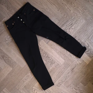 Levis 501 - Svarta Levis 501. Rak passform med smal midja, knappgylf, hårda i materialet. Snyggt slitna med litet hål på vänstra knäet. Liten färgfläck på ena benet (se bild). Osäker på strl men passade mig som brukade ha W23/24 165cm. Skriv gärna för mer info/bilder/mått. Kan skickas mot frakt.