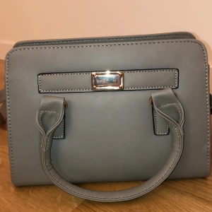 Västa - Snygg grå väska med guld detaljer! Är använd en gång! Den är som sprillans ny! Kom privat för frakt kostnader 