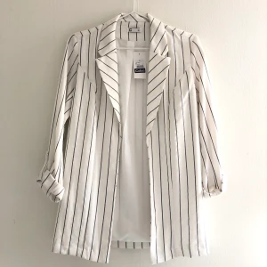 Lång kavaj i svart och vit ränder - Aldrig använd, så prislappen sitter kvar. Den är ungefär till låren och ganska smal i sin form. 