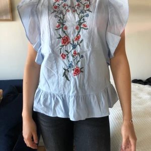 Blus från Zara - Sparsamt använd blus från Zara med sött broderi på magen, öppen i ryggen och volanger. Storlek XS. Finns i Lund/Malmö annars tillkommer frakt