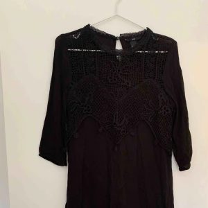  - Rak svart halvkort klänning, halvlånga ärmar med broderade detaljer över bröstkorg. Rak i passform.   Köparen står för porto. 