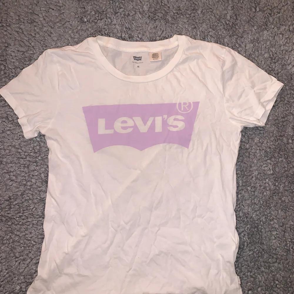 En vit Levis T-shirt med ett rosa/lila Levis märke💕 den sitter hyfsat tajt på och är i mycket bra skick, det är bara å skriva om det är några frågor☺️. T-shirts.