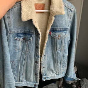 Levisjacka Fodrad - fodrad jeansjacka från levis, storlek L! får plats med en hoodie under och är jätteskön och varm. har knappt använts, inga fläckar eller andra slitningar, som i nyskick! nypris 1299kr