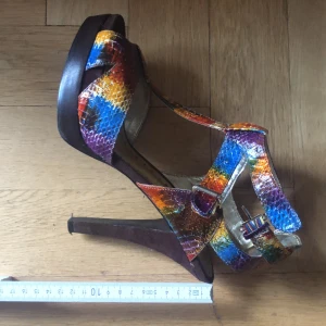 Regnbågsfärgad klackar  - Regnbågsfärgade klackar med mörkbrun klack. Höjd 12 cm. Sparsamt använda! 