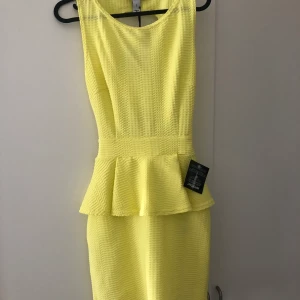 Klänning strl S - Säljer denna klänning som aldrig är använd. Åtsittande med volanger vid midjan i en jättefin gul färg