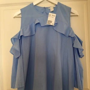  - H&M volangblus i underbar ljusblå färg. 3/4 längd ärm. Oanvänd med prislapp kvar. Storlek 42 men passar mej som vanligtvis har strl 36-38 och är då lite ocersized.