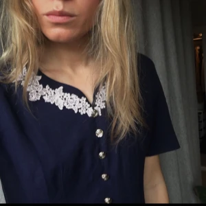  - Superfin knälång klänning, sjömansinspirerad. Guldiga knappar och vit spetts. Dragkedja i ryggen.  Fungerar fint både på sommaren med bara ben och på hösten med strumpbyxor. Frakt tillkommer, kan mötas upp i Stockholm. Betalning sker via swish. 