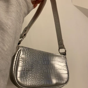 Silvrig axelremsväska!!!! - Fin väska från ASOS, aldrig använd. Helt slutsåld överallt! Frakt tillkommer