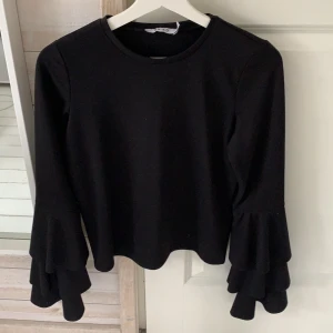 NAKD top - Svart NAKD top med volanger i armarna. Använts väl, är lite noppig på magen men går säkert bort med noppmaskin. Strl XS, skulle säga att den passar folk mellan 160-170cm långa. Hör gärna av dig vid intresse, pris kan diskuteras!