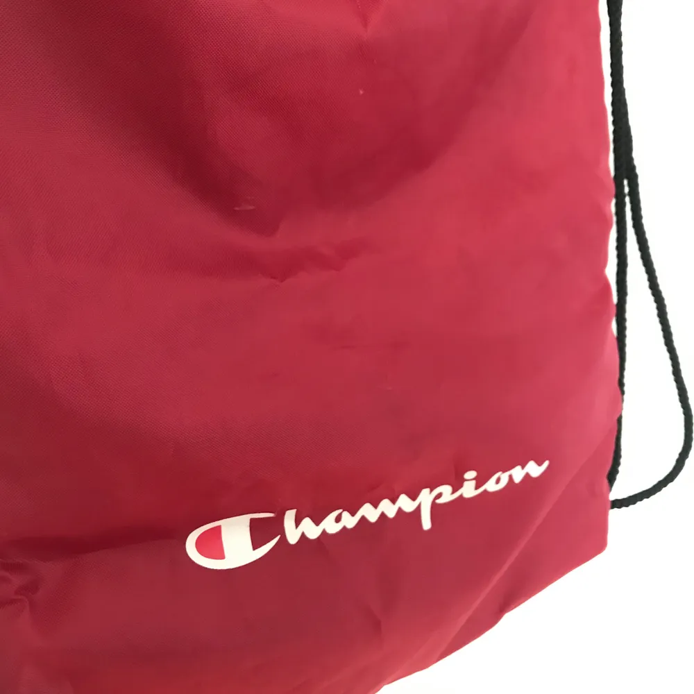 Mörkröd ryggsäck i gympapåse-modell från Champion. Materialet på framsidan har fått en diskret fläck från min vattenflaska(visat på tredje bilden) annars felfri, inga hål. Frakt på 44kr✌. Väskor.