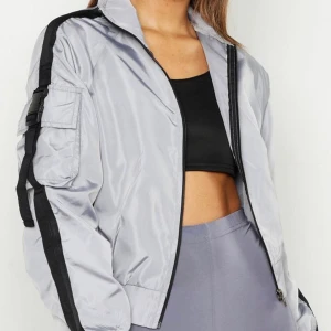 Vindjacka grå med svarta detaljer  - En helt oanvänd vindjacka som tyvärr vart för liten för mig. Jackan har en svart rand på båda armarna och en ficka på högersida. Man kan även anpassa bandet på höger sida som ni ser på bilden. Den är alltså helt ny och väldigt populär då den är utsåld för tillfället. Orginalpris 450kr, pris kan diskuteras!