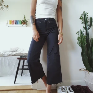 Ankellånga vida jeans med kontrastsömmar - Ett par skitsnygga ankellånga stretchiga jeans i delvis återvunnet material. Hög midja och vida ben. Färgen är grå/svart med vita sömmar. Storlek 36 men passar mig som vanligtsvis är 38! Frakt inräknat i priset 