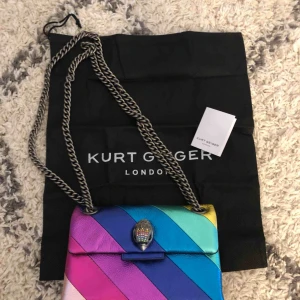  - Säljer min rainbow stripe mini shoulder bag från Kurt Geiger (äkta). Köpt i London maj 2019. Nypris 1530kr säljes nu för 1000kr. Äkta läder. Lite skavd på den cerise färgen, se bild. Köparen står för frakten.   