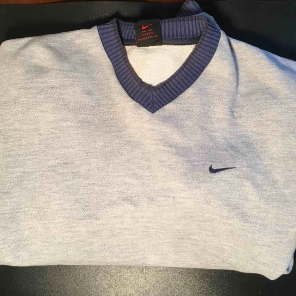 En mysig grå Nike sweater med blå rand på ärmarna och v-hals. OBS! På sista bilden ser man två små vid halsen, men inget man tänker på eller syns tydligt.. Hoodies.