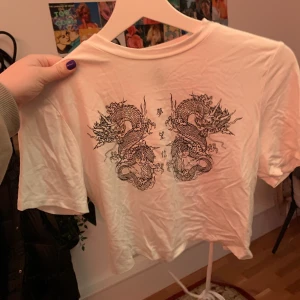 Vit topp med drakar - Vit topp med drakar på från H&M, tröjan har en knytning i ryggen och är helt oanvänd så den är i jättefint skick! Köparen står för frakt!