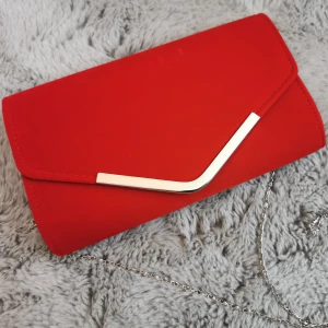 Kuvertväska  - Fin väska i nyskick. Lapp sitter kvar. Den är i rött sammetsliknande tyg. Kan användas både som en axelremsväska och som en clutch. Kedjan kan tas av.