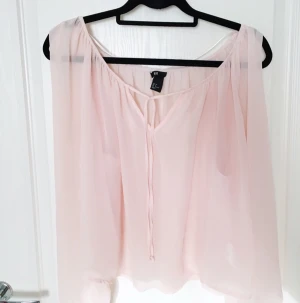  - Rosa transparent blus med "öppna" armar som knyts ihop vid handleden. Lite sliten vid magen pga. feltvättad en gång, men inget som syns på längre avstånd.
