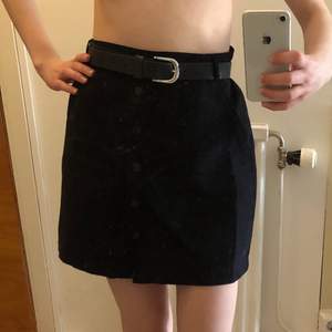 En svart kort kjol i mockaimitation, med fickor och knappar. Inköpt på Nelly. Bältet ingår ej. Möts upp i Uppsala eller skickar på posten! 