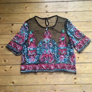 Transparent topp i mesh med broderat bohemiskt mö - Topp i svart mesh med broderat mönster i blommigt. Transparent, men inte där mönstret är. Helt oanvänd och i toppskick! 