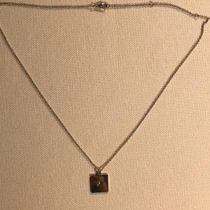 Halsband  - Ett guldfärgat halsband med en fyrkantig berlock med en liten stjärna/sol och en diamant i. 