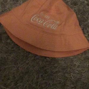 H&M fiskehatt - En fin fiskehatt! Från H&M, Har nästan aldrig använd, Coca cola märke, inga fläckar, besh rosa, köparen står för frakt! 
