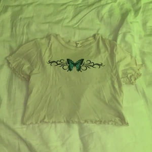 Tröja - En kort vit magtröja med fjärils tryck där framme. Väldigt fin i armarna och därnere, säljer pågrund av att den inte kommer till andvändning längre! Frakt 30 kr. Ändas frakta!