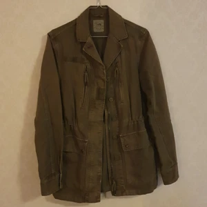 Zara militärjacka - Ofodrad jacka med flera militärdetaljer, oliv-militärgrön färg, 100% bomull, lite lätt stentvättad, knappt använd, dragsko i midjan, metalldragkedja, plastknappar, 2 bröstfickor, 2 höftfickor, stl. XS men lite oversized så kan passa någon i stl. S också.
